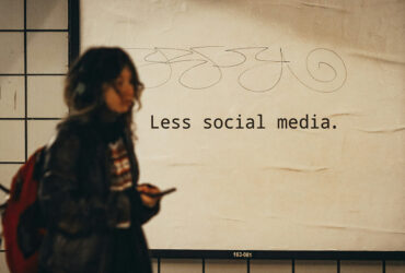 Person mit Smartphone vor Plakat mit Aufschrift "Less Social Media"